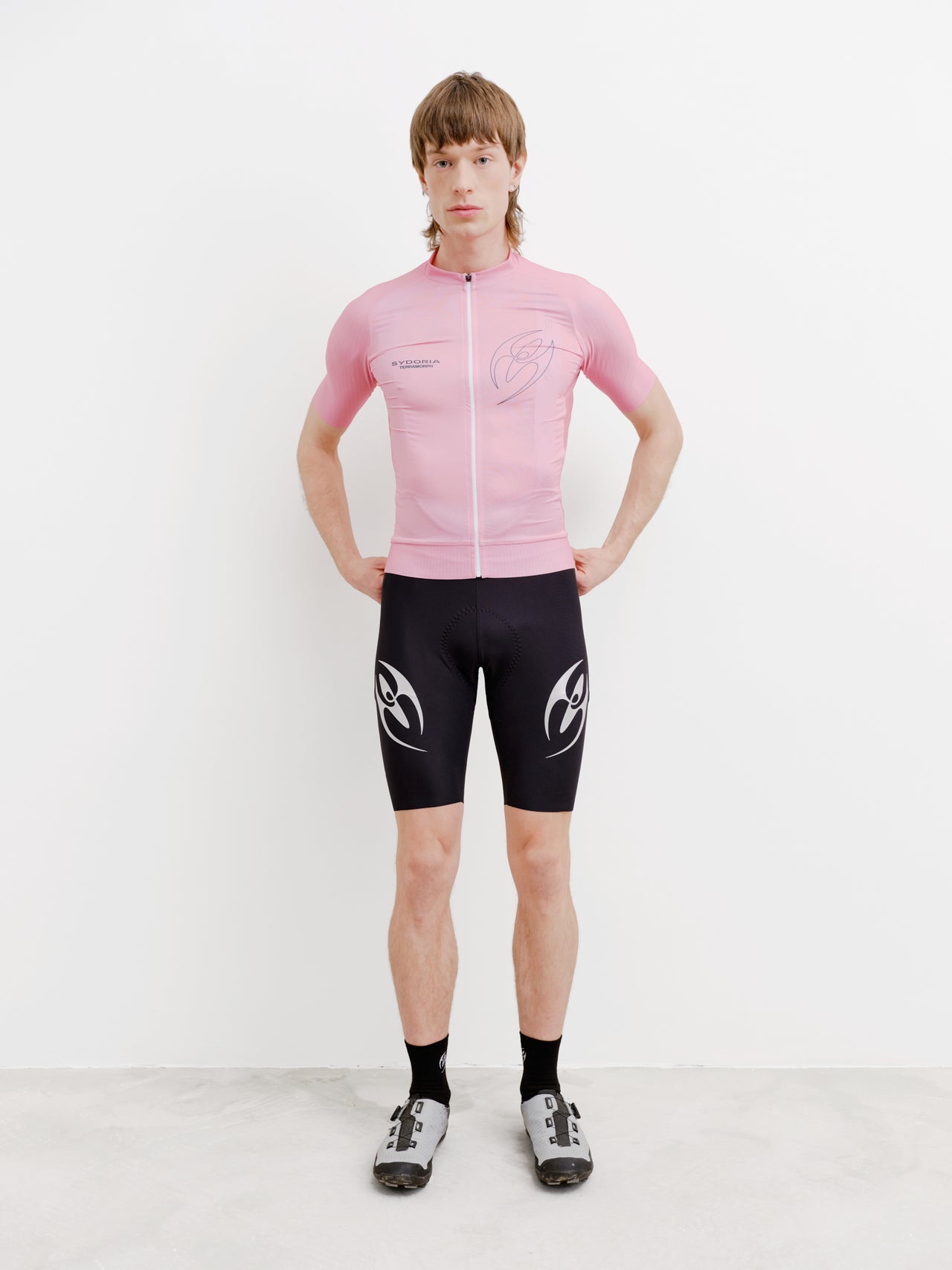 Person wearing a pink cycling jersey and black shorts with a logo on a white background